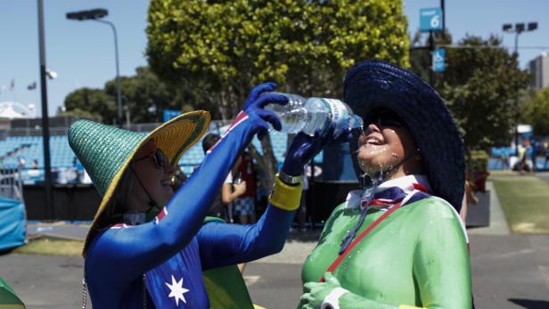 Zwei Personen in Australien-inspirierten Kostümen erfrischen sich mit Wasser an einem sonnigen Tag.