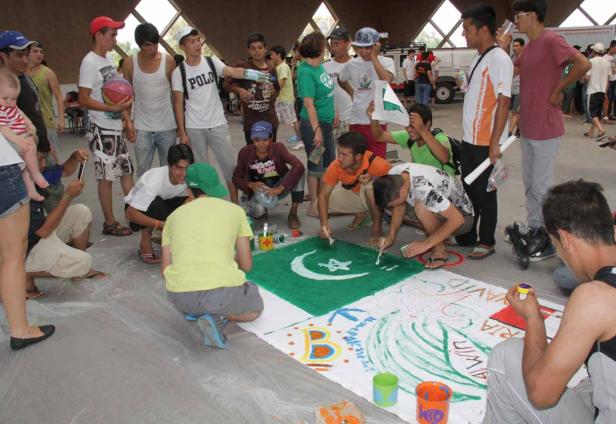 Eine Gruppe junger Leute malt eine große pakistanische Flagge auf eine Plane.