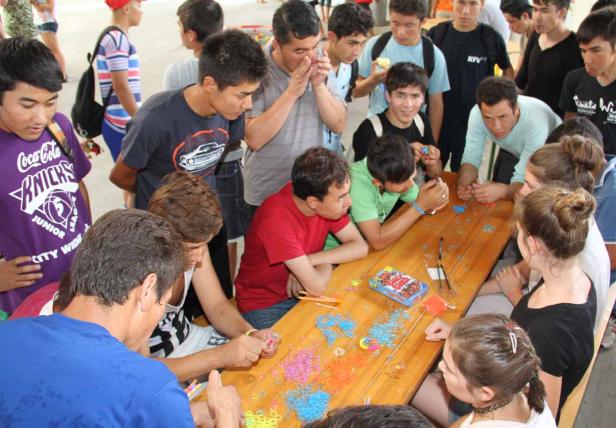 Eine Gruppe junger Leute bastelt gemeinsam an einem Tisch mit bunten Gummibändern.