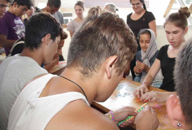 Eine Gruppe von Menschen sitzt an einem Tisch und bastelt mit bunten Gummibändern.