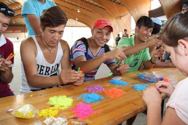 Eine Gruppe junger Leute bastelt mit bunten Gummibändern an einem Tisch.