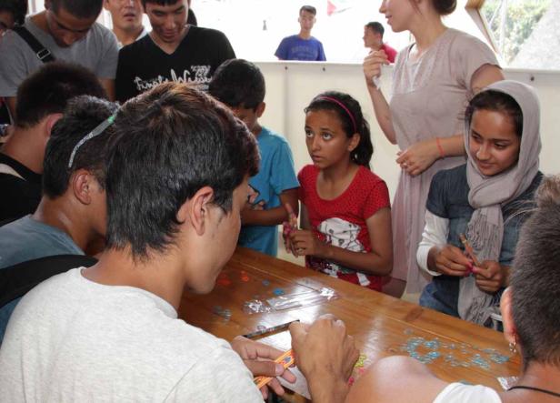 Eine Gruppe junger Menschen sitzt an einem Tisch und bastelt mit Gummibändern.