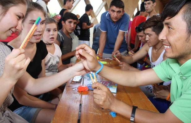 Eine Gruppe junger Leute sitzt an einem Tisch und bastelt mit Stiften und Gummibändern.