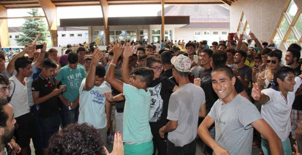 Eine große Gruppe junger Männer versammelt sich in einem Gebäude und einige halten ihre Handys hoch.