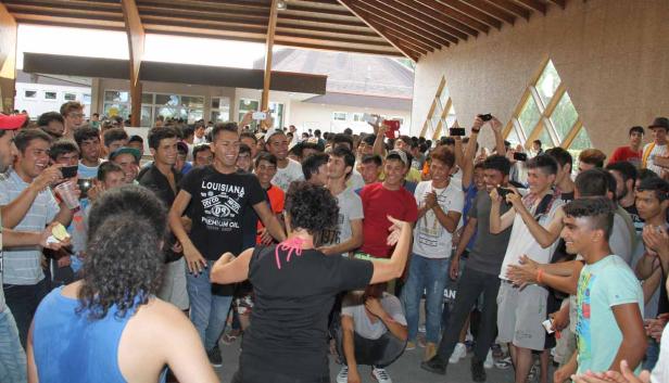 Eine Frau tanzt vor einer Gruppe junger Männer, die sie anfeuern und filmen.