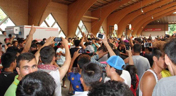 Eine große Menschenmenge in einer Halle mit Holzbalkendecke hält ihre Handys hoch.