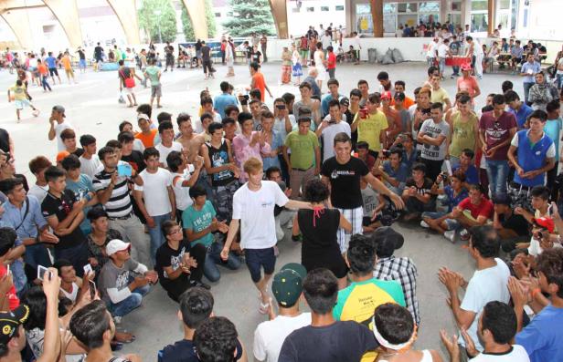 Eine große Gruppe junger Leute versammelt sich im Freien, einige tanzen, andere schauen zu.