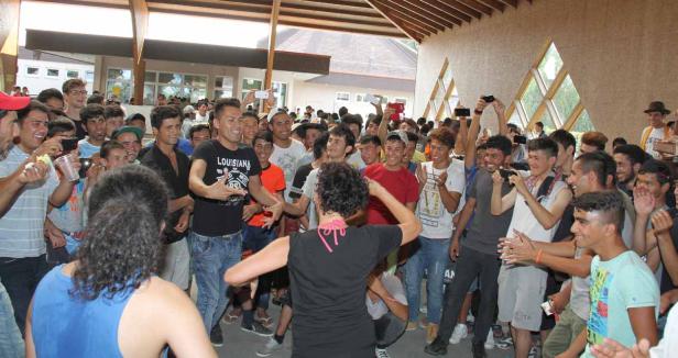 Eine Frau tanzt vor einer großen Gruppe junger Männer, die sie anfeuern und filmen.