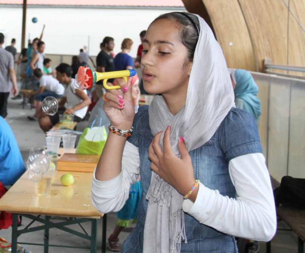 Ein Mädchen mit Kopftuch pustet Seifenblasen mit einer gelben Tröte.