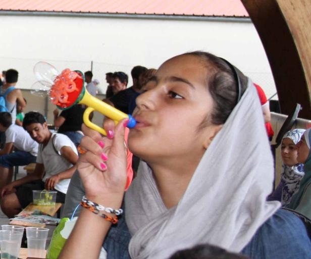 Ein Mädchen mit Kopftuch pustet in ein gelbes Seifenblaseninstrument.