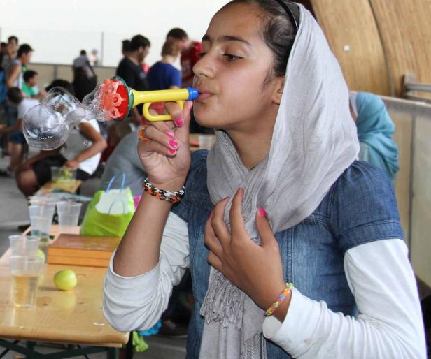 Ein Mädchen mit Kopftuch pustet mit einem Spielzeug Seifenblasen.