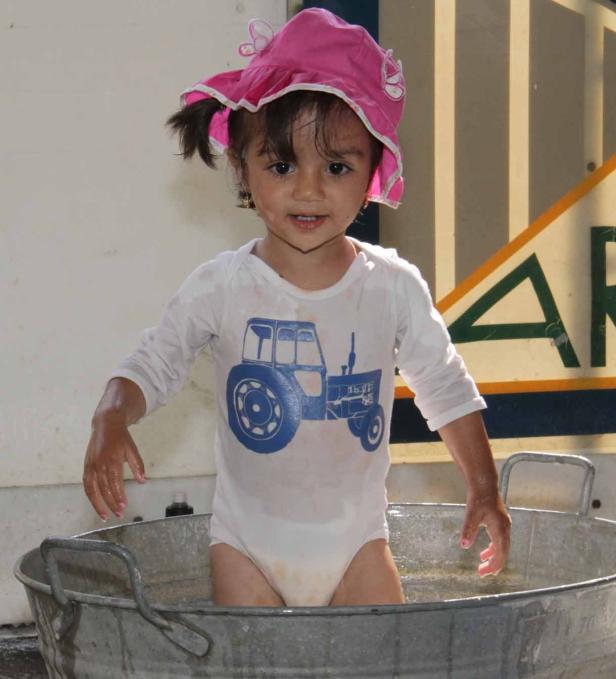 Ein kleines Mädchen mit rosa Hut badet in einer Zinkwanne.