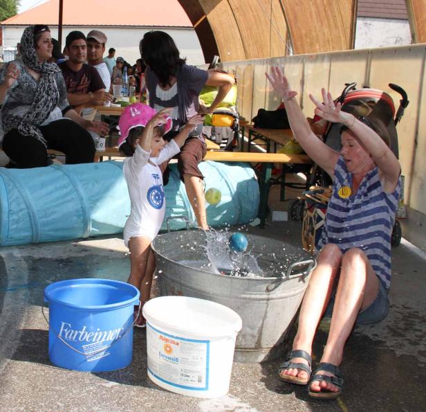 Ein Mädchen wirft einen Ball in einen Eimer Wasser, während eine Frau daneben sitzt und die Hände hebt.