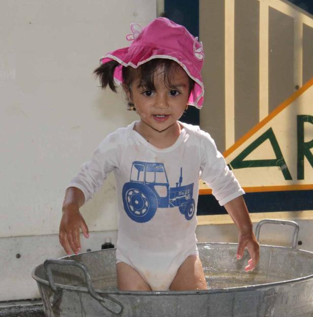 Ein kleines Mädchen mit rosa Hut badet in einer Zinkwanne.