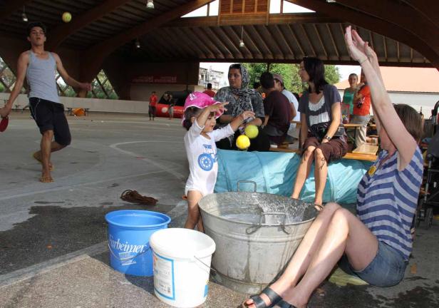 Eine Gruppe von Menschen, darunter ein Kind, das mit Wasser und Bällen spielt, während andere zuschauen.