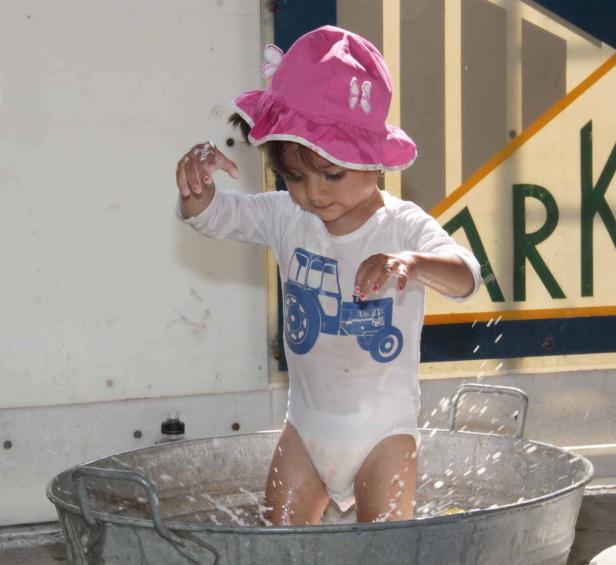 Ein kleines Mädchen mit rosa Hut planscht in einer Zinkwanne.