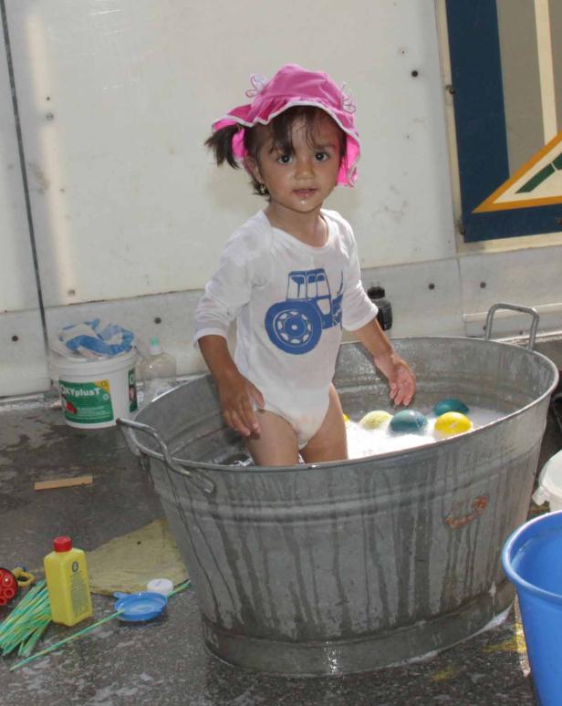 Ein kleines Mädchen mit rosa Hut badet in einer Zinkwanne.
