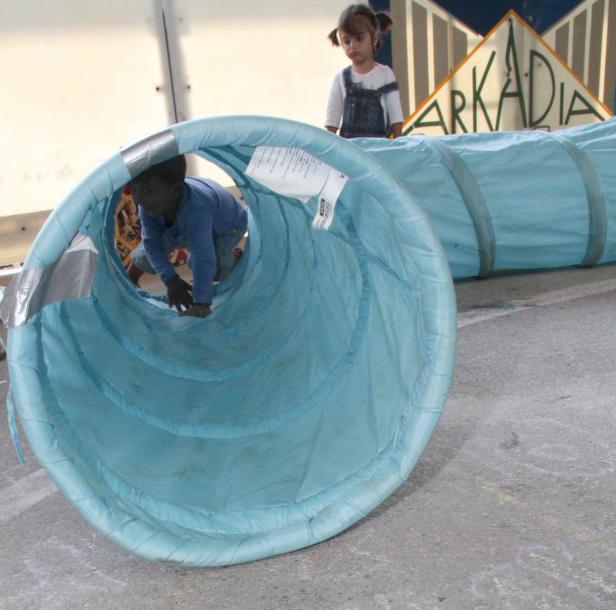Ein Kind krabbelt durch einen blauen Tunnel, während ein anderes Kind zusieht.