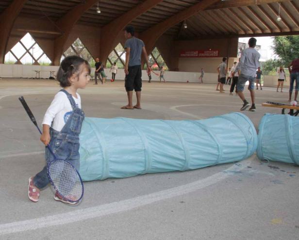 Ein kleines Mädchen steht mit einem Badmintonschläger neben einem blauen Tunnel.
