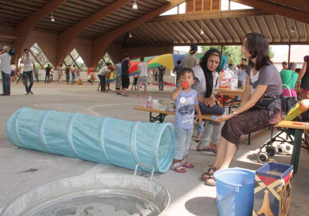 In einer Halle spielen Kinder, während Erwachsene zusammensitzen.