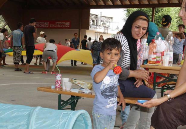 Ein kleiner Junge spielt mit einem Spielzeug, während eine Frau mit Kopftuch daneben sitzt.