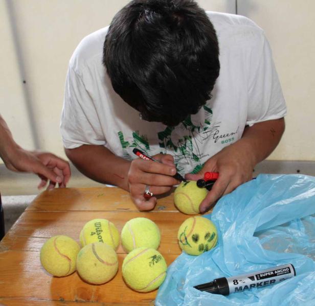 Eine Person bemalt Tennisbälle mit einem schwarzen Stift.
