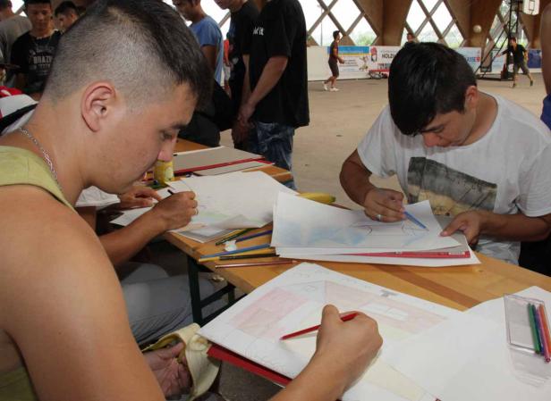 Mehrere Personen sitzen an Tischen und zeichnen mit Buntstiften auf Papier.