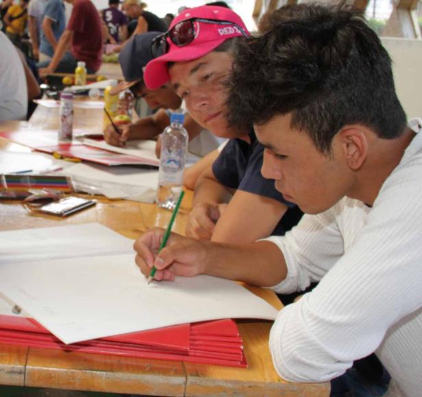 Mehrere Personen sitzen an einem Tisch und zeichnen auf Papier.