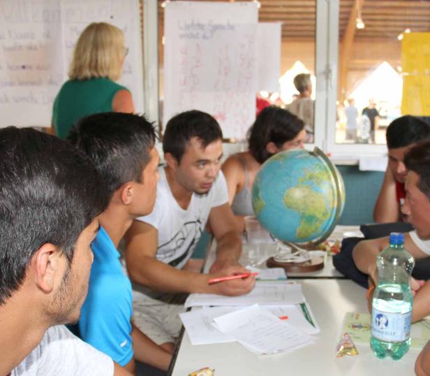 Eine Gruppe junger Leute sitzt an einem Tisch mit einem Globus und diskutiert.