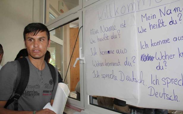 Ein Mann steht vor einem Fenster mit einem Plakat, das deutsche Sätze zeigt.