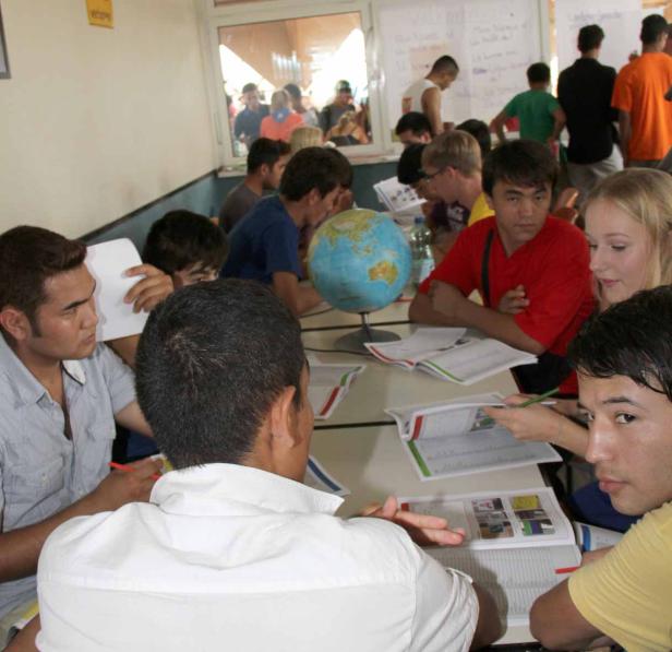 Eine Gruppe junger Leute sitzt an einem Tisch mit einem Globus und bearbeitet Schulbücher.