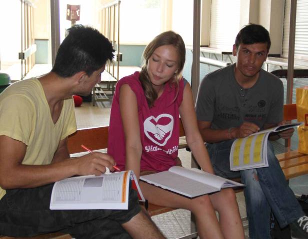 Drei junge Leute sitzen auf einer Bank und lernen mit ihren Unterlagen.