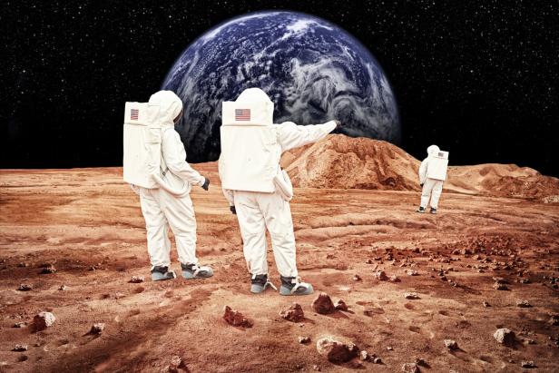 Drei Astronauten stehen auf der Oberfläche eines roten Planeten und blicken zur Erde.