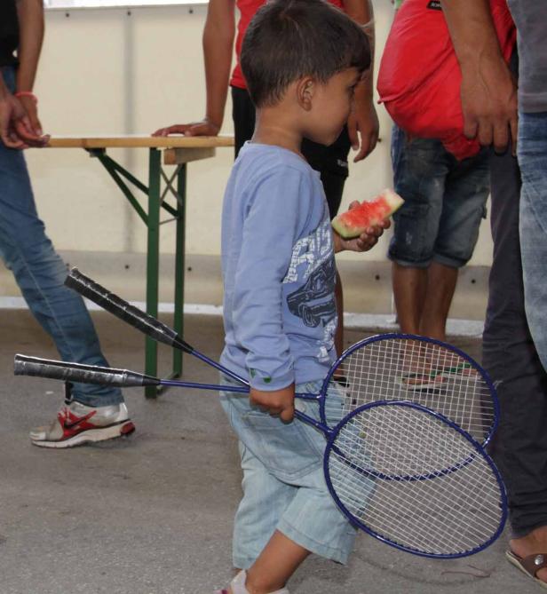 Ein Junge hält eine Scheibe Wassermelone und mehrere Badmintonschläger.