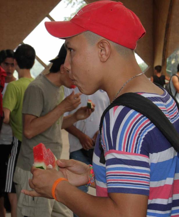 Ein junger Mann mit roter Kappe isst ein Stück Wassermelone.