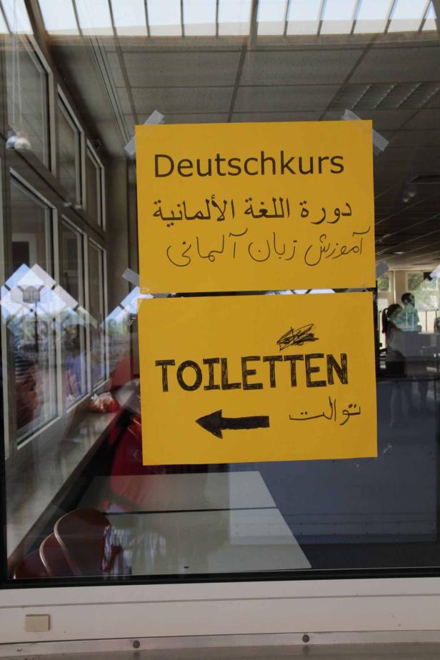 Gelbe Schilder an einer Tür weisen auf einen Deutschkurs und Toiletten hin.