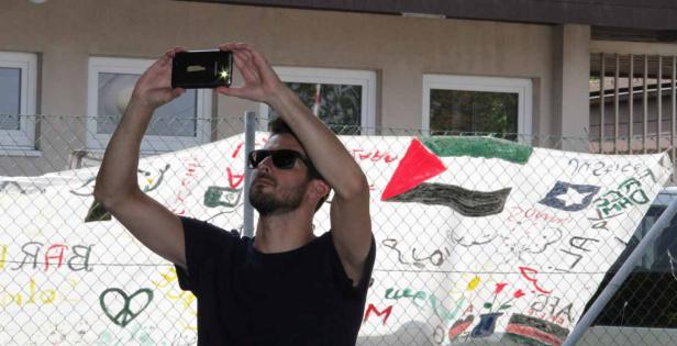 Ein Mann mit Sonnenbrille fotografiert ein Transparent mit Zeichnungen und Symbolen.