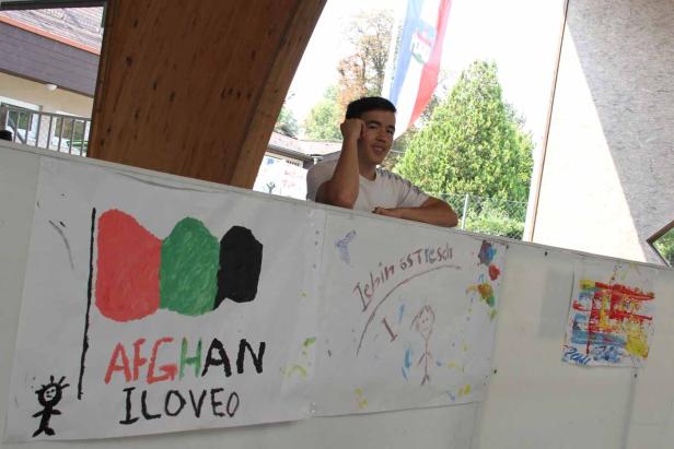 Ein junger Mann steht hinter einem Banner mit einer Zeichnung der afghanischen Flagge.