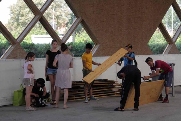 Eine Gruppe von Menschen arbeitet mit Holz unter einem ungewöhnlichen Dach.