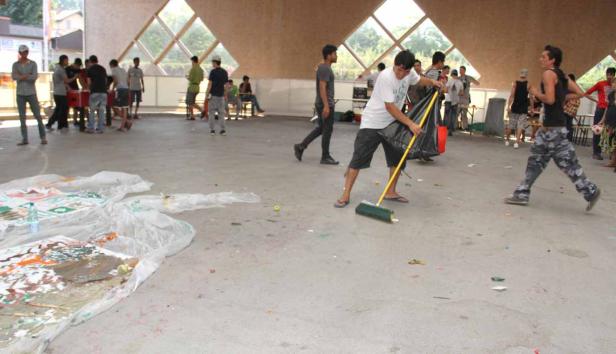 Ein Mann kehrt den Boden in einer Halle, während andere sich im Hintergrund aufhalten.