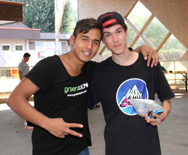 Zwei junge Männer posieren lächelnd mit einem Arm um die Schulter des anderen für ein Foto.