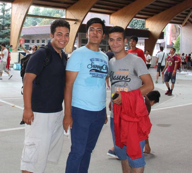 Drei junge Männer posieren für ein Foto auf einem belebten Platz.