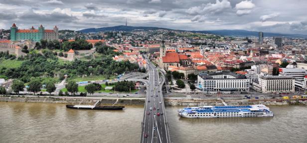 Blick auf Bratislava mit Burg, Donau und Brücke bei bewölktem Himmel.