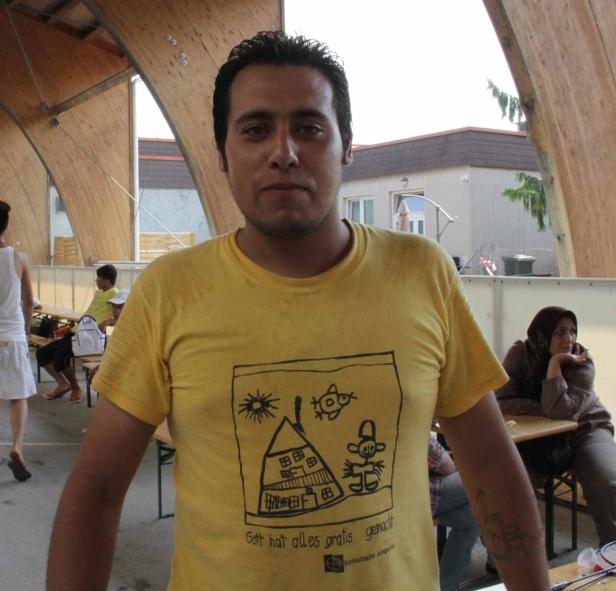 Ein Mann mit gelbem T-Shirt steht vor einem Gebäude.