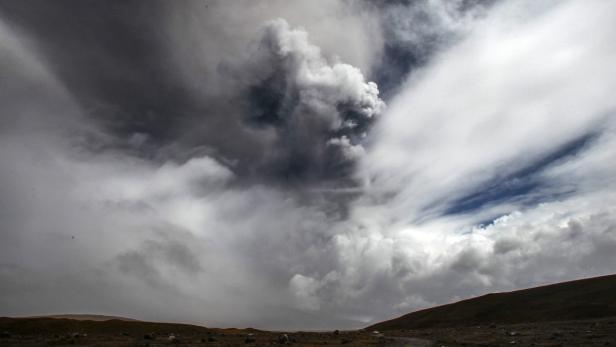 Dramatischer Himmel mit dunklen Wolken über einer hügeligen Landschaft.