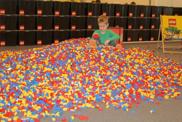 Ein Junge sitzt in einem Berg von roten, blauen und gelben Legosteinen.