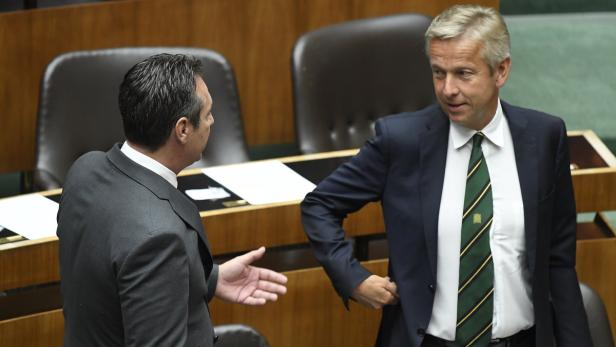 Zwei Männer in Anzügen unterhalten sich in einem Sitzungssaal.