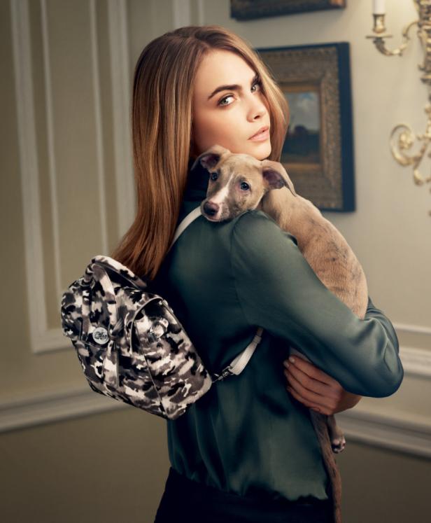 Cara Delevingne hält einen Welpen im Arm und trägt einen Rucksack.