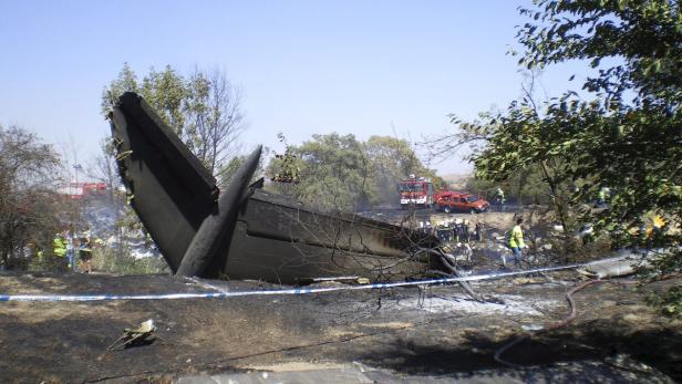 Die Überreste eines Flugzeugabsturzes mit Feuerwehrleuten und Absperrband an der Absturzstelle.