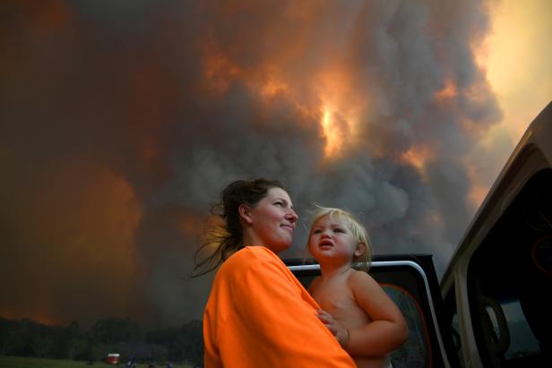Sharnie Moren and her 18-month-old daughter Charlotte look on as thick smoke rises from bushfires near Nana Glen